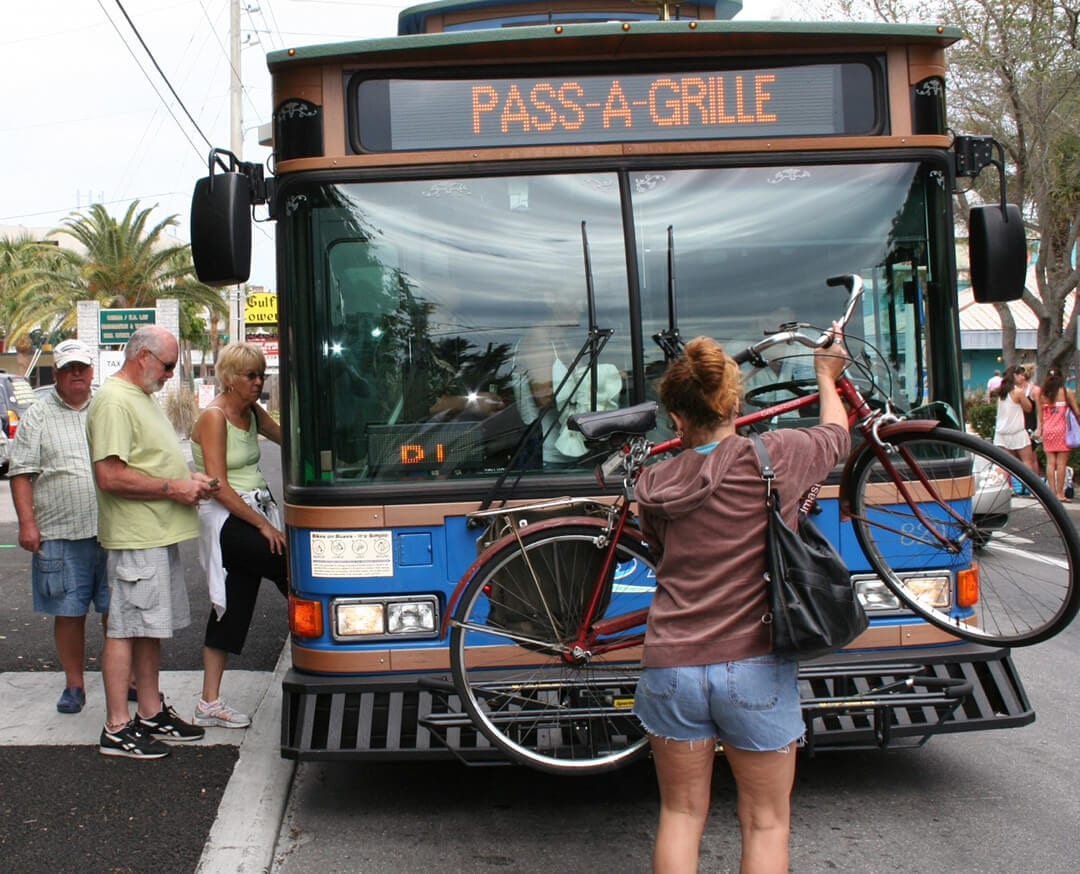 Woman placing bicycle on front of county bus. People stepping into the bus.