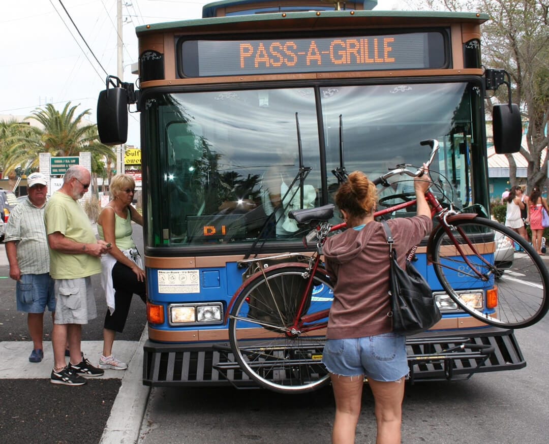 Woman placing bicycle on front of county bus. People stepping into the bus.